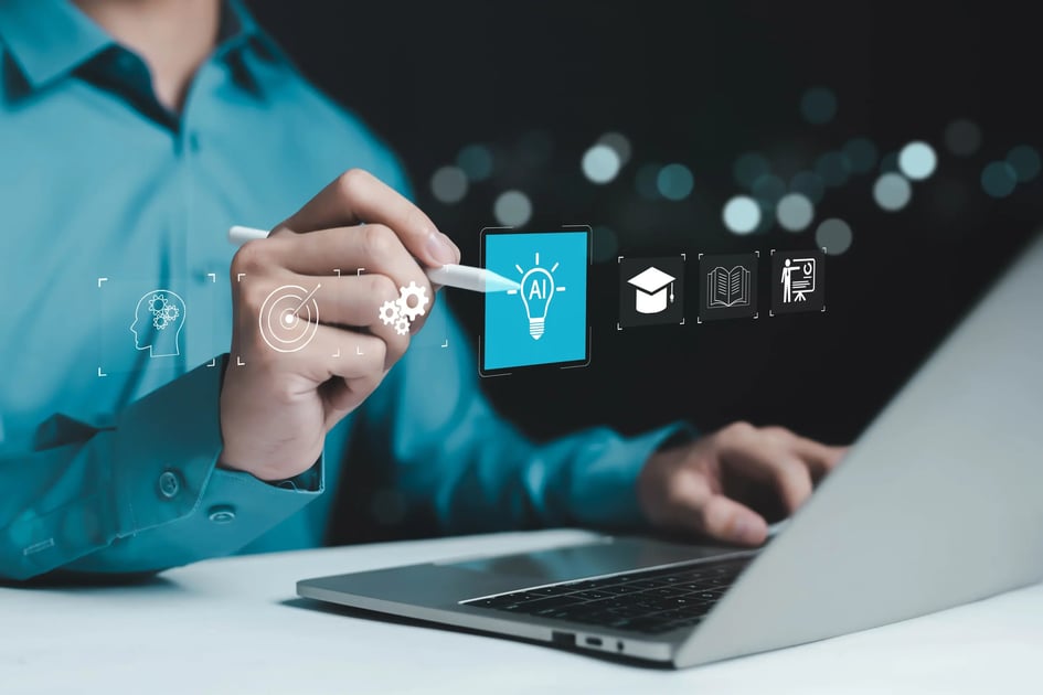 A person at a laptop points a stylus at an AI lightbulb, with icons for thinking, a goal, learning, and teaching.
